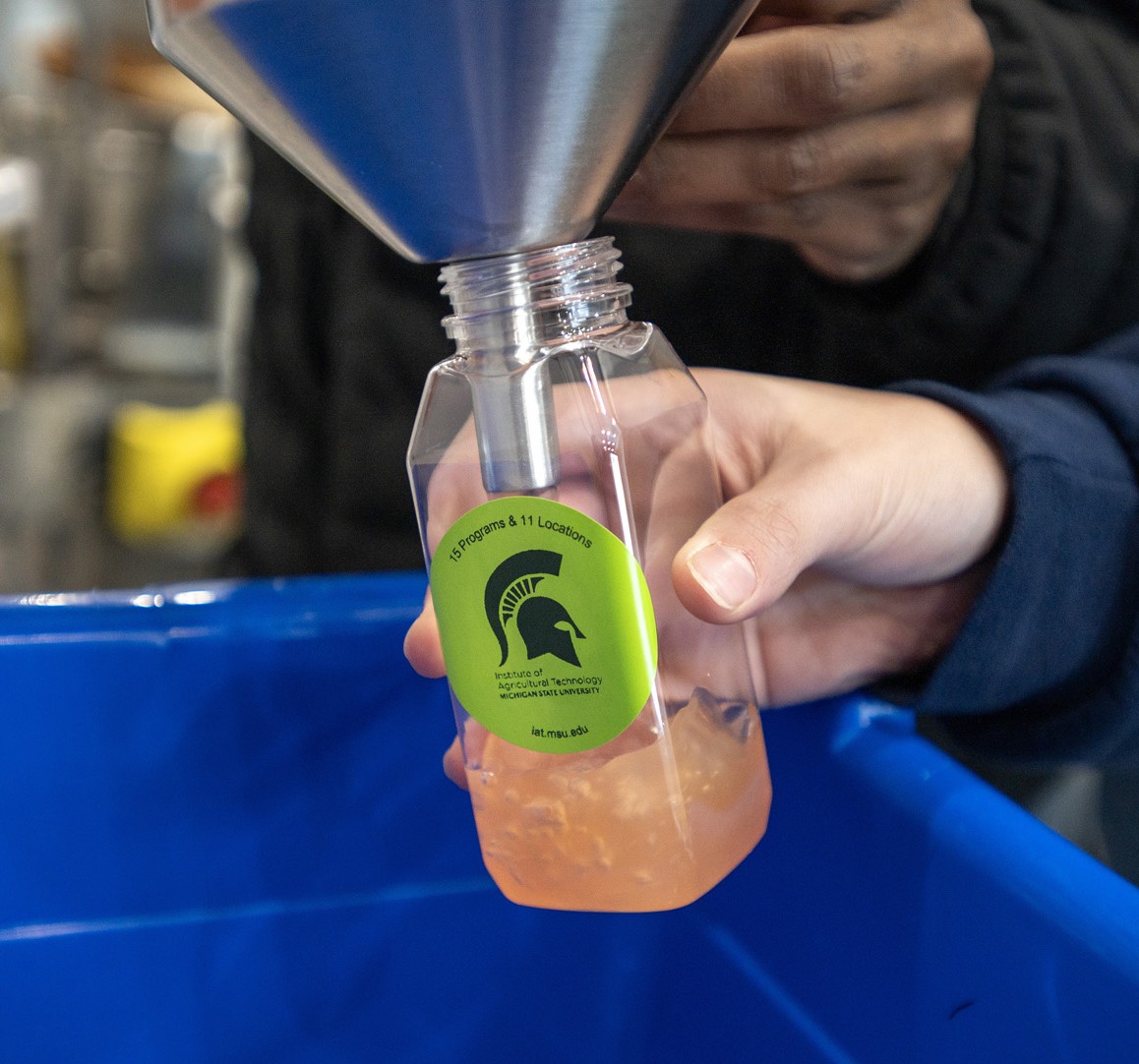 A participant pours processed food product into a labeled bottle during a hands-on demonstration inside Michigan State University&rsquo;s mobile food processing lab.